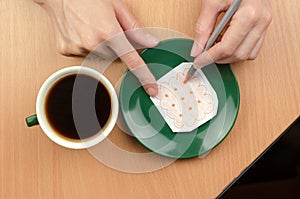 A cup of coffee and a painted cookie on a saucer. A woman`s hand draws a cookie