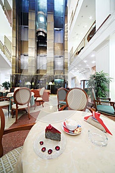 Cup of coffee and piece of cake on table in hall on big hotel