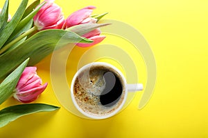 Cup of coffee and pink tulips on yellow background, top view