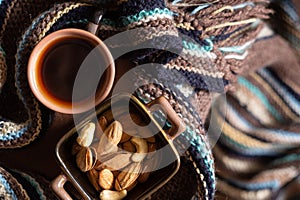 Cup of coffee, plate with nuts, book and warm scarf