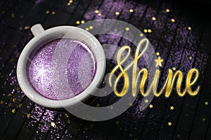 Cup of coffee with purple glitter on dark background with golden