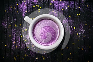 Cup of coffee with purple glitter on dark background with golden