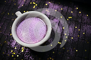 Cup of coffee with purple glitter on dark background with golden