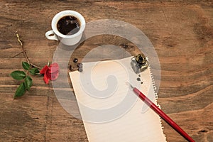 Cup of coffee with red rosebud and pen on white paper.