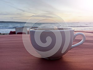 A cup of coffee on red table with calm sunset view over the sea. Relax with beach view. Weekend coffee.