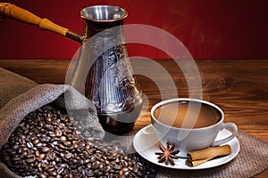 Cup of coffee with roasted beans and turkish coffee pot on wooden table