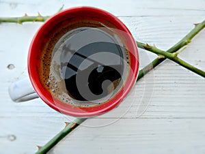 Cup of coffee with a rose thorn on a white rustic background