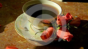 A cup of coffee with roses on a saucer.