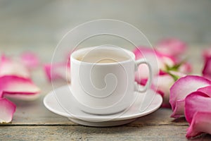 Cup of coffee on rustic wooden table in a frame of pink roses. G