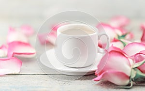 Cup of coffee on rustic wooden table in a frame of pink roses. G
