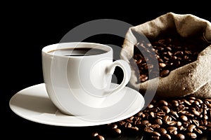 Cup of coffee with saucer with bag with coffee beans on black