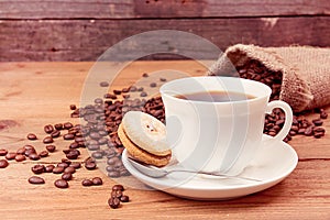 Cup of coffee, saucer with cookies, roasted coffee beans in sack