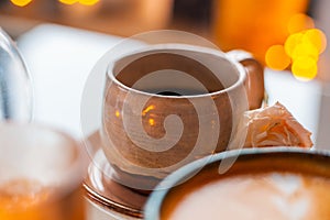 A cup of coffee on a saucer is decorated with roses next to candles in beautiful candlesticks