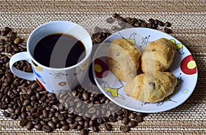 A Cup of coffee is on the scattered coffee beans, next saucer with croissants.