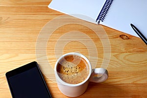 Cup of coffee with smartphone and notebook on wooden table for a concept of teleworking