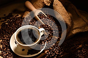 Cup of coffee with smoke and coffee beans on burlap sack