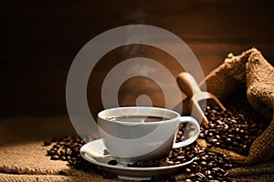 Cup of coffee with smoke and coffee beans on burlap sack on old wooden background