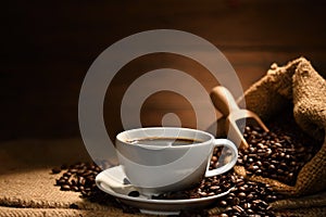 Cup of coffee with smoke and coffee beans on burlap sack on old wooden background