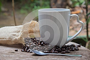 Cup of coffee with smoke and coffee beans in burlap sack on wood