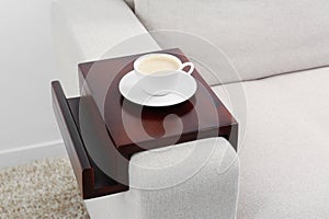 Cup of coffee on sofa with wooden armrest table indoors. Interior element