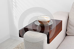 Cup of coffee on sofa with wooden armrest table indoors. Interior element