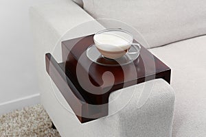 Cup of coffee on sofa with wooden armrest table indoors. Interior element