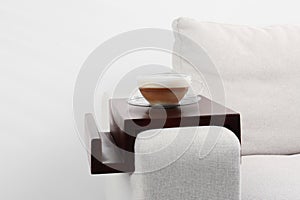 Cup of coffee on sofa with wooden armrest table indoors. Interior element