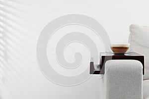 Cup of coffee on sofa with wooden armrest table indoors, space for text. Interior element