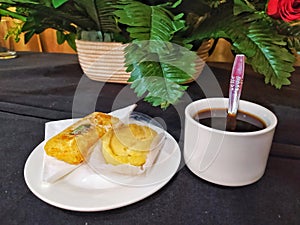 A cup of coffee and some cake with artificial flowers on the black table