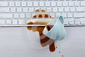 Cup of coffee spilled over keyboard on white wooden table, flat lay