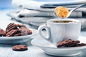 Cup of coffee spoon with cane sugar, chocolate biscuits and the background newspaper.