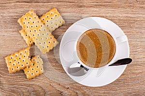 Cup of coffee, spoon on saucer, broken cookie with filling on table. Top view