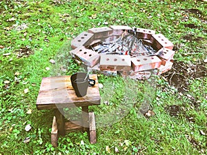 A cup of coffee stands on a stool on the grass near a fire surrounded by bricks.