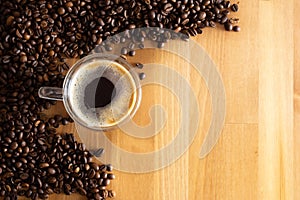 A cup with coffee stands on a wooden table next to scattered coffee beans