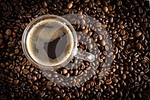 A cup with coffee stands on a wooden table next to scattered coffee beans