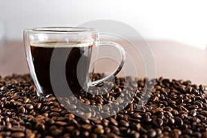 A cup with coffee stands on a wooden table next to scattered coffee beans