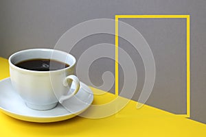 A cup of coffee stands on a yellow and gray background, next to a frame for text.