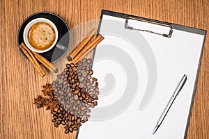 A cup of coffee, star anise, cinnamon and a clipboard