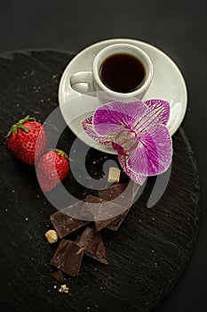Cup of coffee, sugar, strawberries, chocolate on the slate on a black background