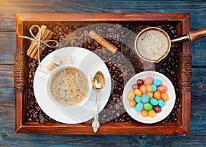 Cup of coffee, sweet in the bowl, coffeepot, cinnamon, anise, sugar, coffee beens on a wooden tray.