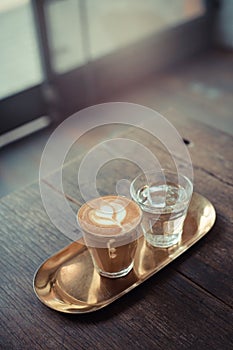 Cup of coffee with sweet silk candy on top on wooden plate over white table with plant in background