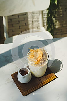 Cup of coffee with sweet silk candy on top on wooden plate over white table with plant in background
