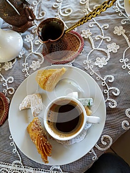 A cup of coffee and sweets on a saucer, coffee in a Turk stand on a white embroidered tablecloth. Crimean Tatar national