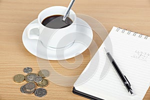 Cup of coffee on table with notepad and coinage