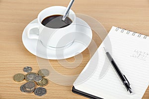 Cup of coffee on table with notepad and coinage photo