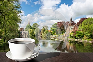 Cup of coffee on the table with view of green park featuring Minnewater Lake and small castle in Bruges during sunny day in spring photo