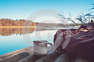 Cup of coffee or tea, backpack of traveller on wooden pier on summer tranquil lake