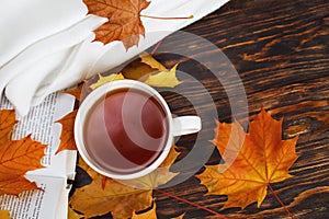 Cup of coffee or tea with golden autumn leaves, plaid and book on a wooden background .top view. Fall concept