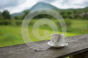 Cup of coffee or tea on a wooden table over mountains landscape and rice field with sunlight. Beauty nature background