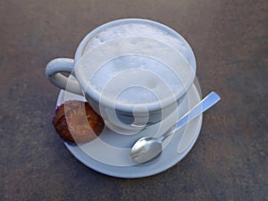 Cup of coffee with teaspoon and small muffin - on the table